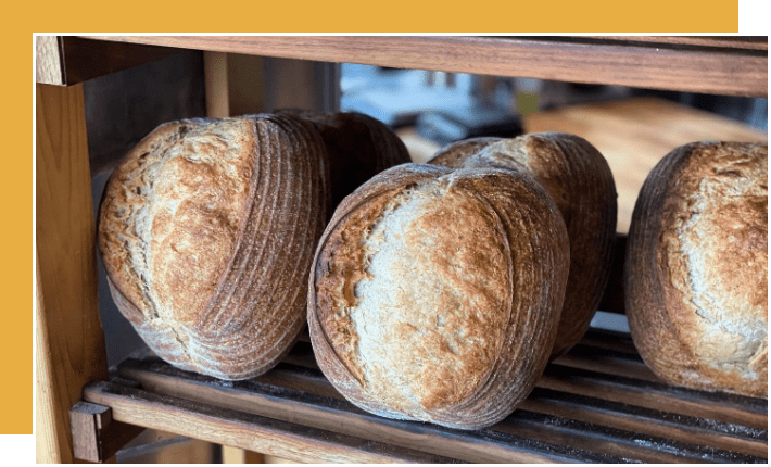 Four loaves of bread sitting on a wooden shelf.